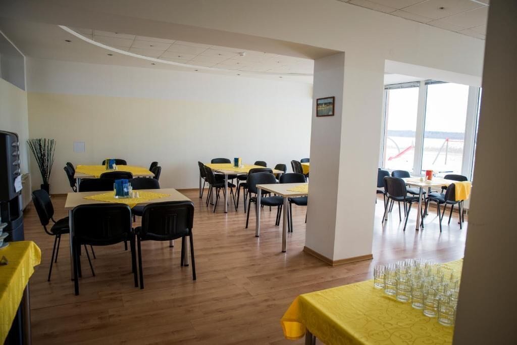 Un salón de conferencias con varias mesas y sillas, un amplio ventanal con vistas, y un mantel amarillo sobre una de las mesas.