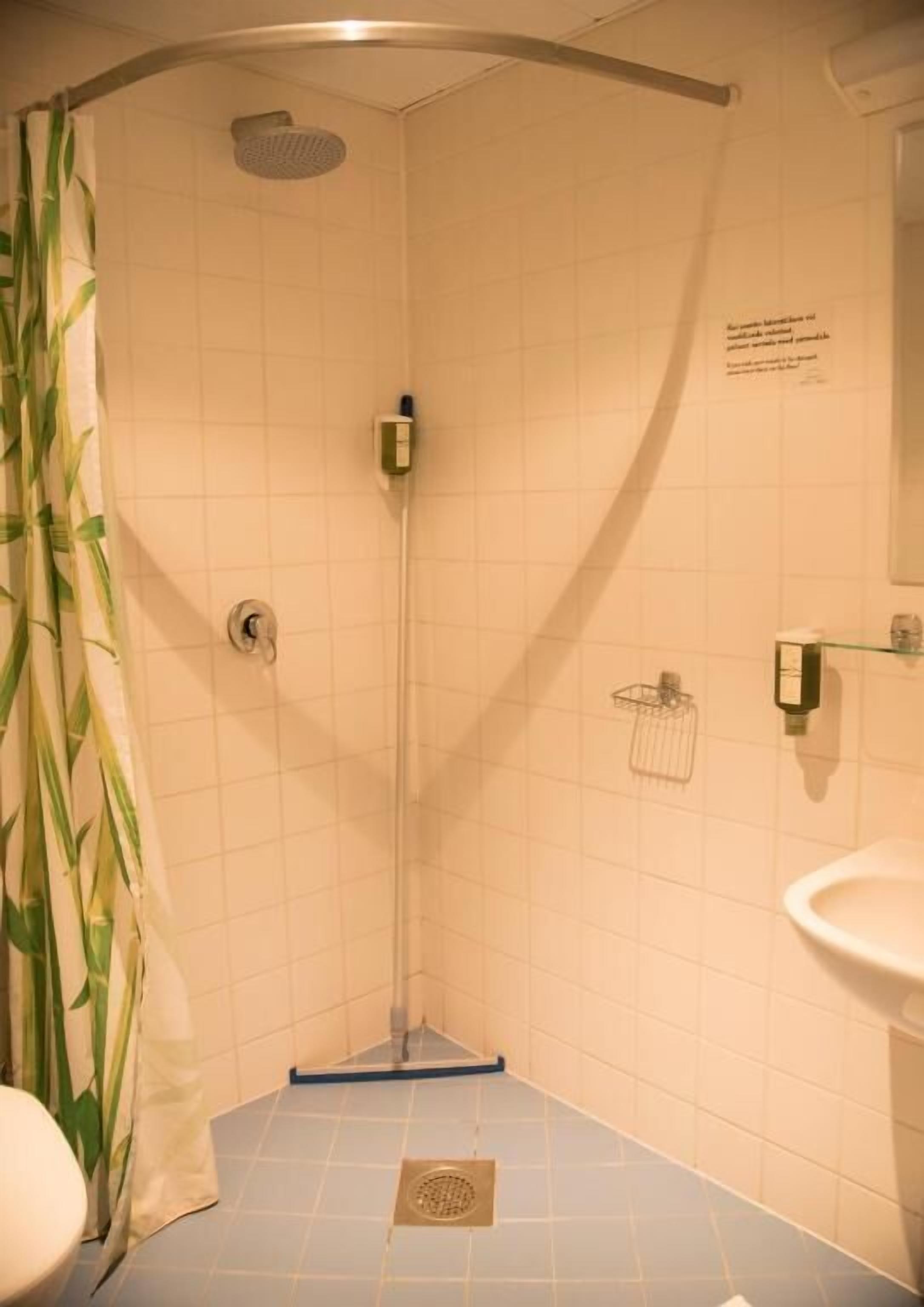 Une petite salle de bain carrelée, équipée d’une douche, de toilettes et d’un lavabo.