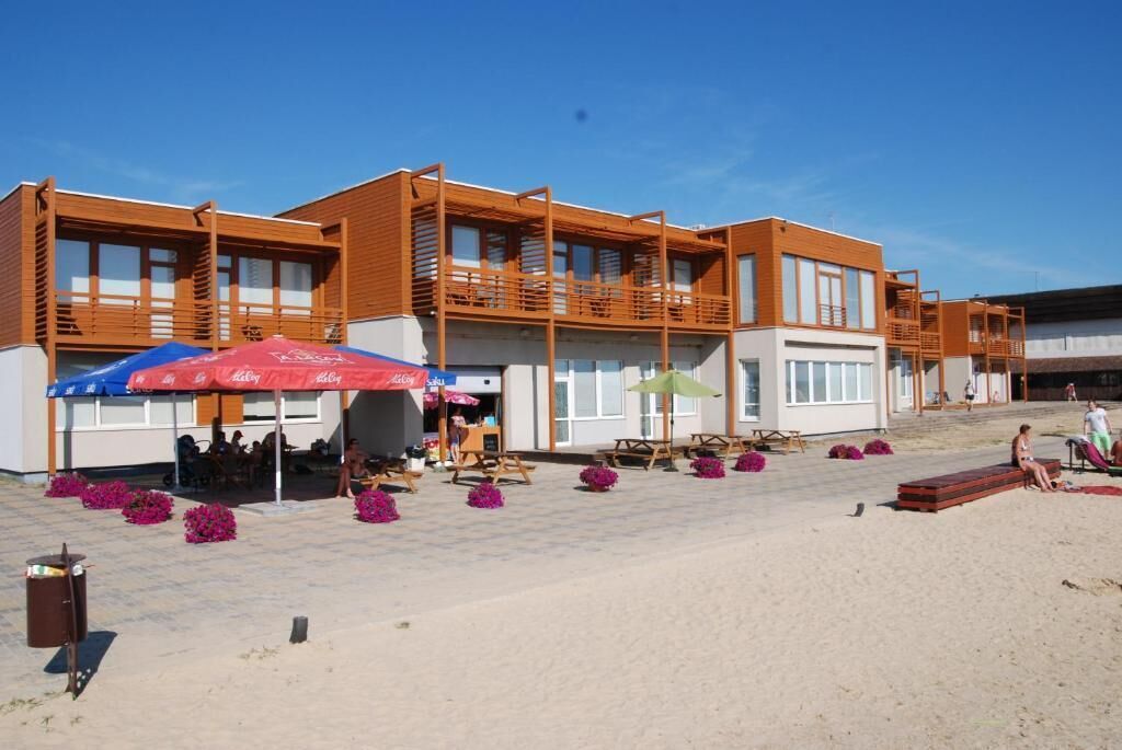 Un bâtiment moderne doté de nombreux balcons, d’un espace extérieur aménagé avec des sièges et d’une zone au sol recouverte de sable.