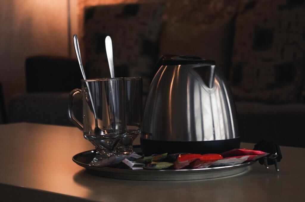 Una tetera eléctrica de acero inoxidable sobre una mesa, junto a una taza de vidrio y una cuchara.
