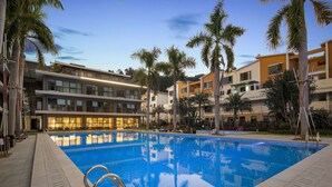 Piscina rodeada de palmeras y edificios modernos con balcones.