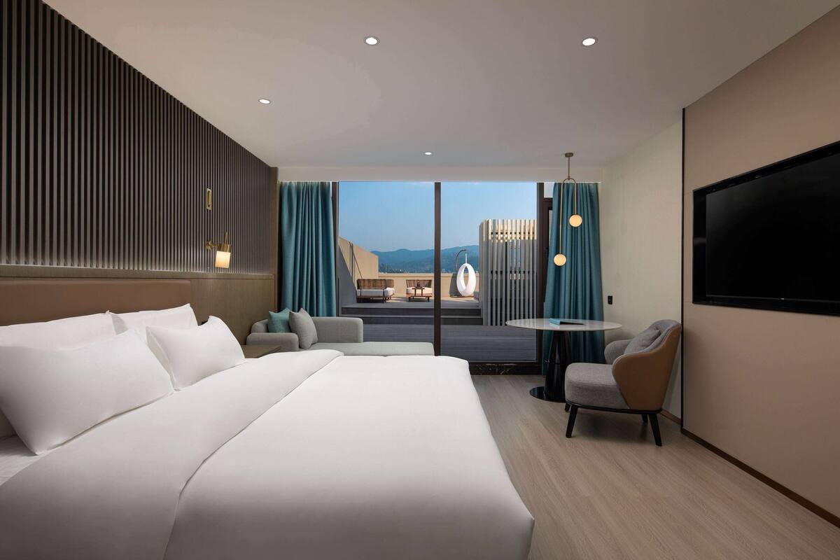 Une chambre d’hôtel moderne avec un grand lit, un coin salon avec une table et un téléviseur fixé au mur.