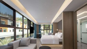 Una habitación de hotel moderna con una cama grande, un sofá, una mesita y un televisor.