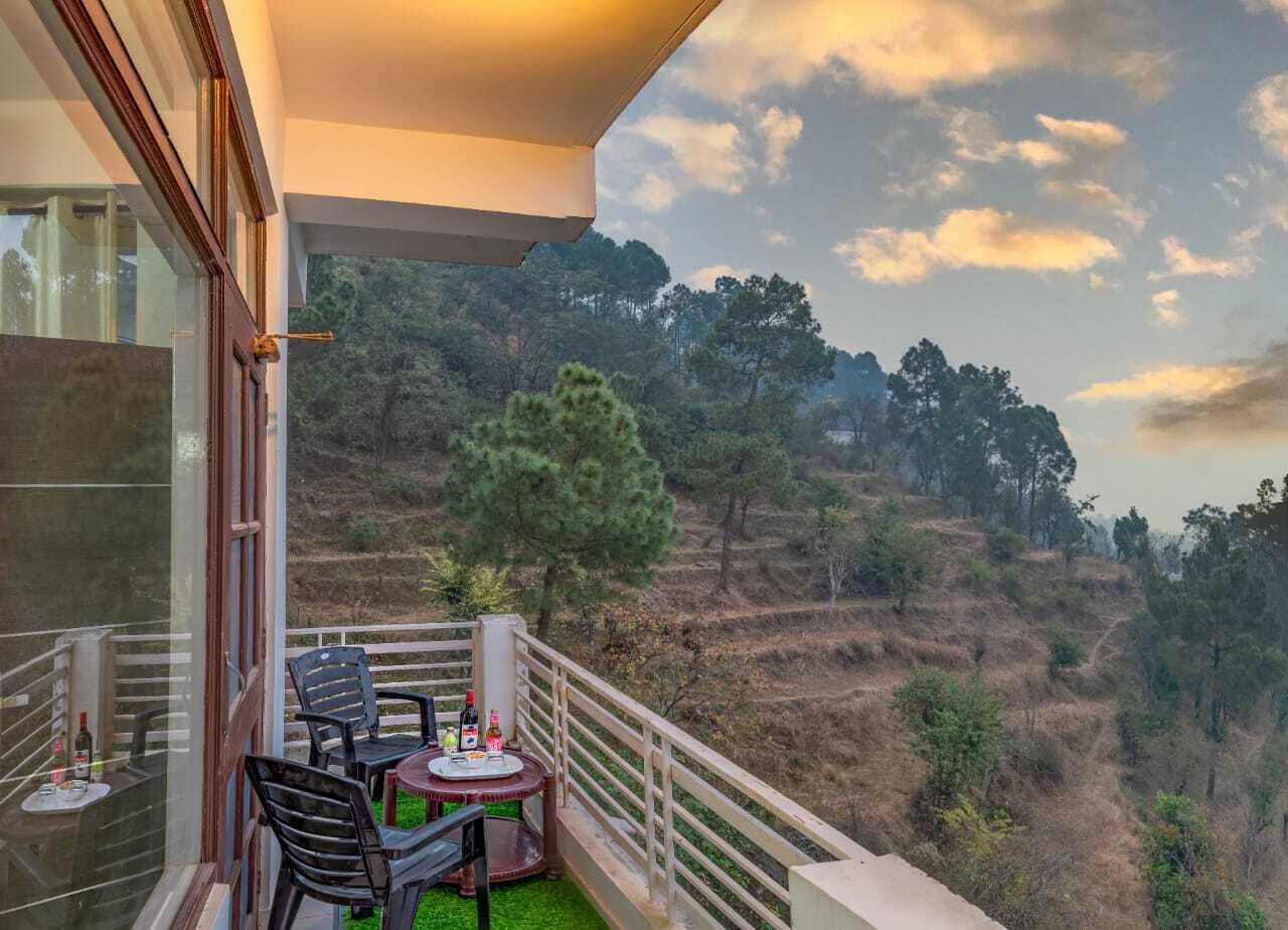 Un balcón con mesa y sillas, con vista a un paisaje montañoso y árboles.
