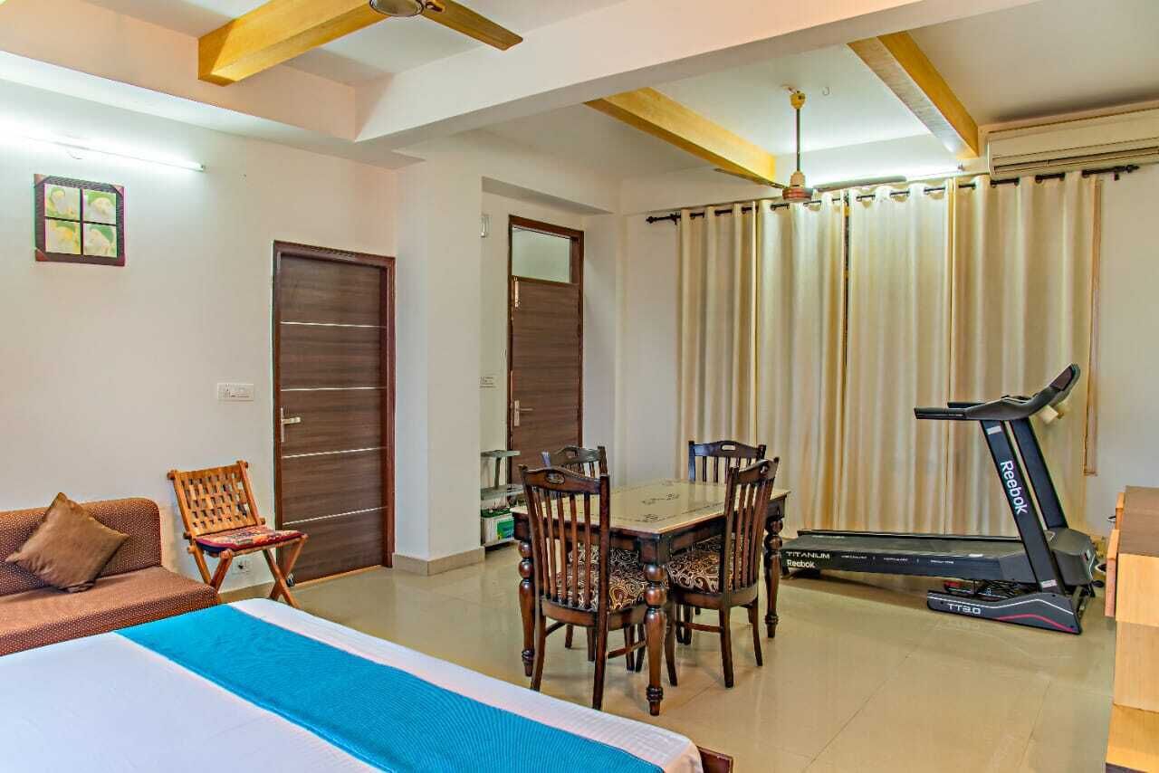 A hotel room with a bed, a dining table with chairs, a treadmill, and a ceiling fan.