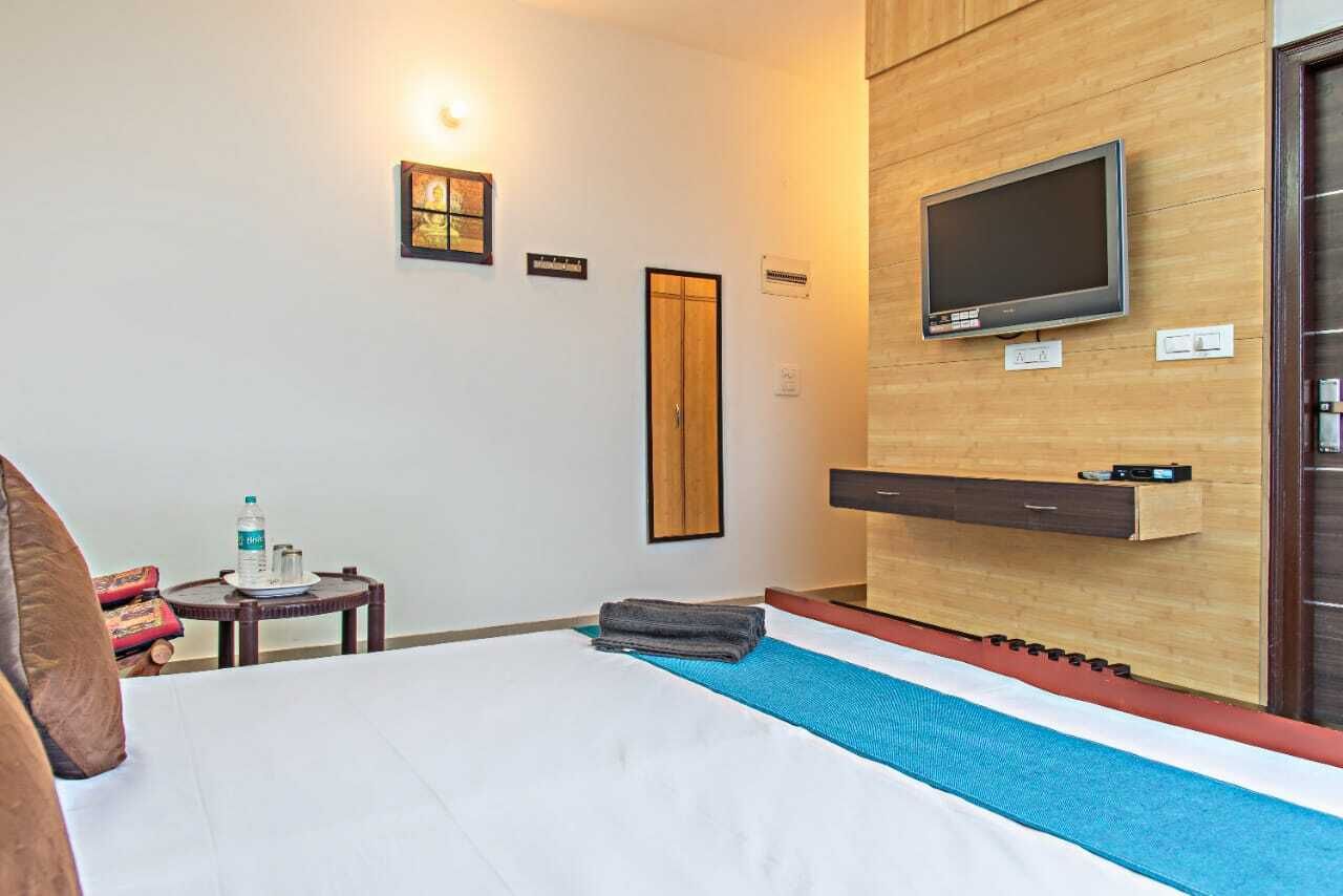 A hotel room with a bed, a TV mounted on the wall, a small table with a bottle and glasses, and a door.