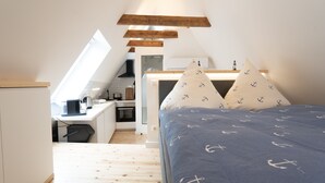 Une chambre à coucher de taille réduite, avec un lit, des oreillers et une vue sur la cuisine et la salle à manger, grâce à une porte ouverte.