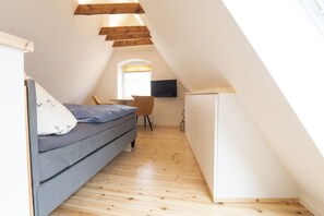 A compact, well-lit attic bedroom with a bed, a desk, and a TV. - Cozy attic apartment in the old town WLAN 100Mbit (Stralsund)