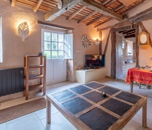 Una habitación rústica con vigas de madera a la vista, una chimenea de piedra, un televisor y una mesa con mantel rojo.