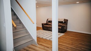 Una habitación amplia con piso de madera, un sillón de cuero y una escalera con barandas de madera.