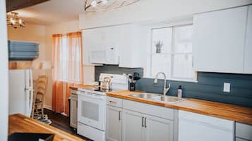A modern kitchen with white cabinets, a wooden countertop, a built-in oven, and a dishwasher.