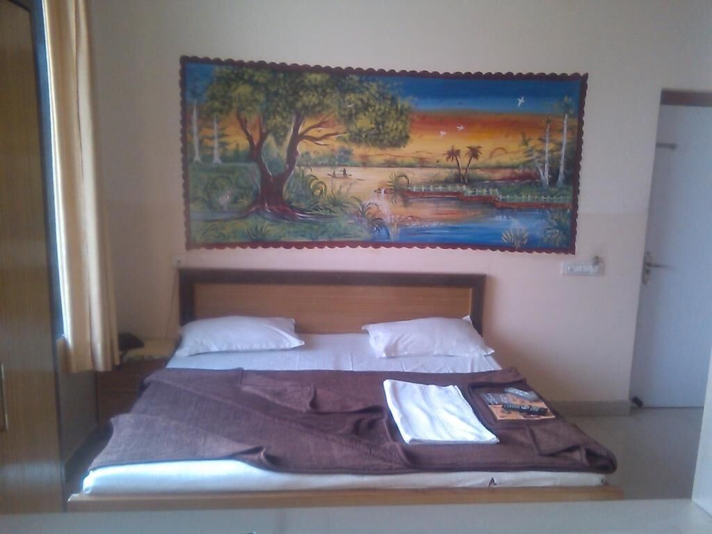 Un lit avec des oreillers blancs et une couverture marron, un tableau représentant un paysage au-dessus, et une porte sur la droite.