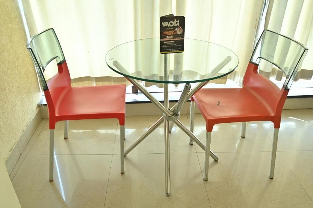 Une table en verre, deux chaises rouges, un présentoir à menus et une fenêtre avec des rideaux.