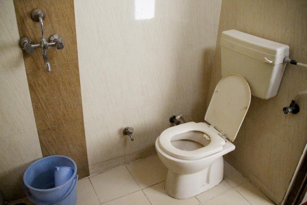 Pieni kylpyhuone, jossa on wc, sininen ämpäri ja suihkupää.