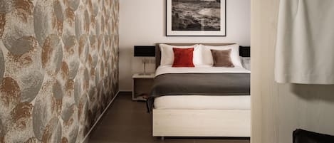 A bedroom with a bed, a nightstand, a framed picture on the wall, and a patterned wall.