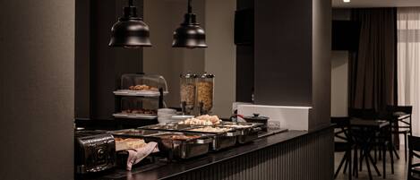 A buffet area with multiple food stations, a coffee machine, and hanging pendant lights.