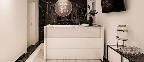 Un hall d’hôtel moderne avec un sol en marbre, un comptoir d’accueil, un téléviseur et une plante.