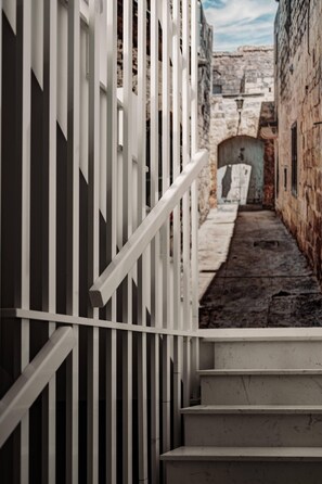 A narrow stone corridor with a white railing and steps leading to an arched doorway. - Urban Isle (Gzira)
