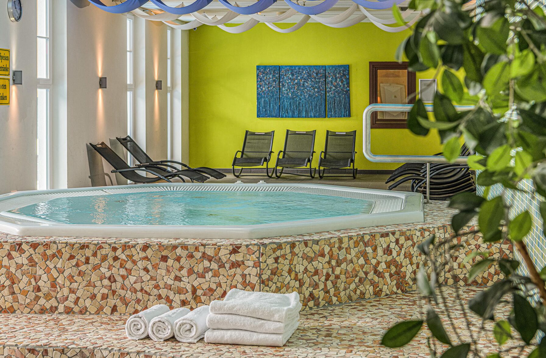 Un área de piscina con borde de mosaicos, sillas de descanso y un cartel que indica prohibido fumar y consumir bebidas alcohólicas.