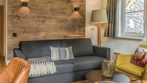 Ein modernes Wohnzimmer mit einem dunkelgrauen Sofa, einer Holzwand, einer Lampe und einem Fenster mit Vorhängen.