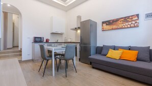 Eine moderne Küche mit Essbereich, ein graues Sofa mit orangefarbenen Kissen und einem Gemälde an der Wand.