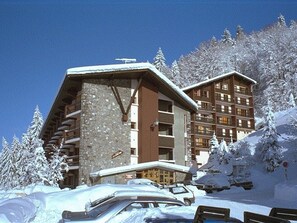 Um hotel de vários andares com fachada de pedra e seção superior de madeira, rodeado por árvores cobertas de neve.