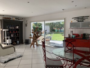 Une cuisine moderne avec une table à manger en verre, des chaises rouges et une vue sur le jardin grâce à de grandes portes coulissantes.