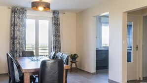 A dining area with a wooden table and black chairs, a potted plant, and a view of the outdoors through large windows. - Large house with pond and sea view, near the Lighthouse, garden and terraces, parking (Gatteville-le-Phare)