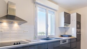 A modern kitchen with dark cabinetry, a stainless steel range hood, a double sink, and a window providing natural light. - Large house with pond and sea view, near the Lighthouse, garden and terraces, parking (Gatteville-le-Phare)