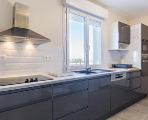 A modern kitchen with dark cabinetry, a stainless steel range hood, a double sink, and a window providing natural light.
