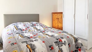 Een slaapkamer met een bed met een beddegoed met een patroon, een houten garderobe en een witte kast.