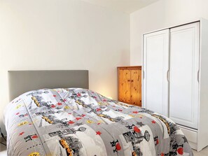 Un dormitorio con una cama cubierta por una colcha estampada, un armario de madera y un armario blanco.