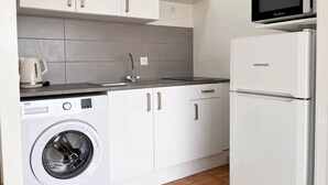 Een compacte keuken met witte kasten, een ingebouwde wasmachine, een koelkast en een magnetron.