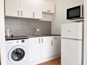 Una cocina compacta con armarios blancos, lavadora integrada, refrigerador y microondas.