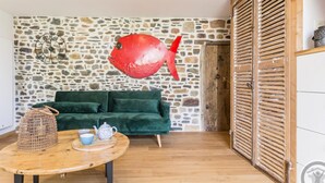 Um quarto aconchegante com parede de pedra, sofá verde, mesa de madeira com chaleira e xícaras, e uma decoração de peixe vermelho.