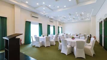 A conference room with multiple round tables, white chairs, and a podium.
