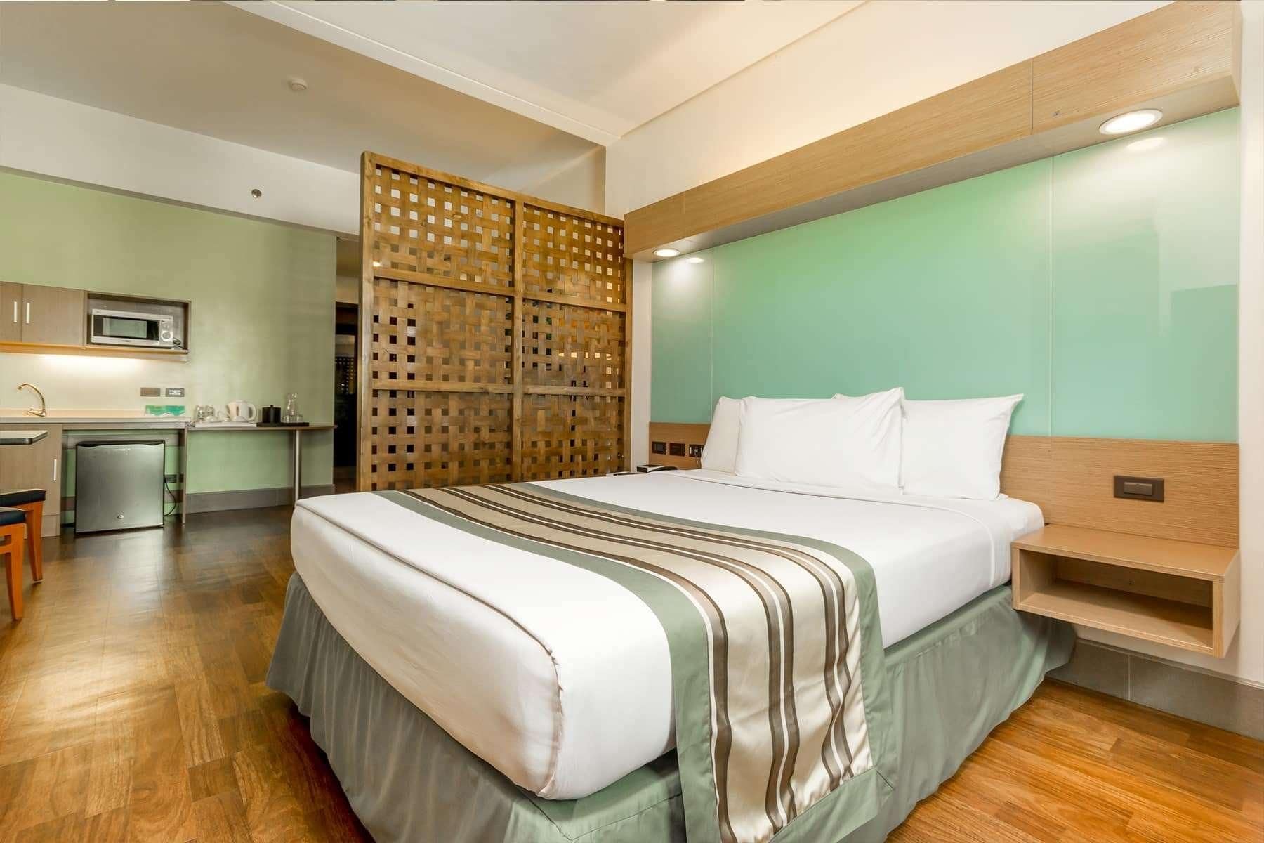 A hotel room with a bed, a desk, a microwave, and a refrigerator.
