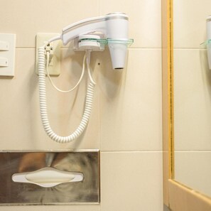 Een haardroger bevestigd aan een muur, met een stopcontact en een metalen voorwerp eronder.