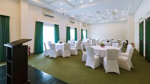 Une salle de conférence avec des tables rondes, des chaises blanches, un pupitre et des rideaux verts.