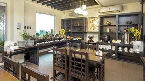 Un restaurant avec des meubles en bois, une longue table commune et des étagères où sont exposées de la vaisselle et des objets de décoration.