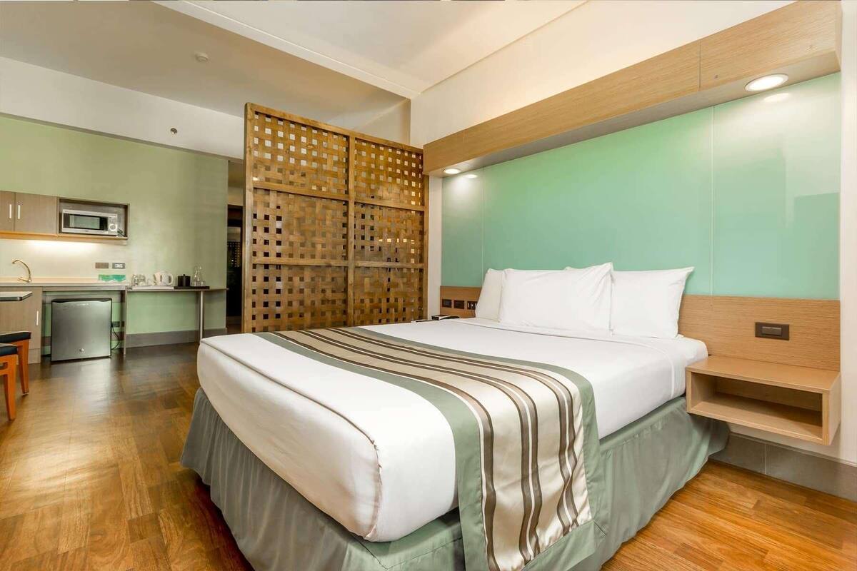 A hotel room with a bed, a desk, a microwave, and a refrigerator.