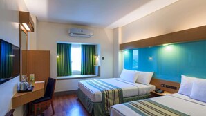 Une chambre d’hôtel avec deux lits, un bureau, une chaise, une fenêtre avec des rideaux, un climatiseur et une table de chevet avec un téléphone.