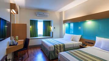 A hotel room with two beds, a desk, a chair, a window with curtains, an air conditioning unit, and a nightstand with a phone.