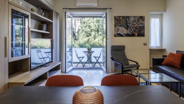 A modern living room with a dining area, a balcony with outdoor furniture, and a large painting on the wall.