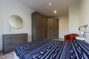 A bedroom with a bed, a dresser, a wardrobe, a mirror, and a chair.