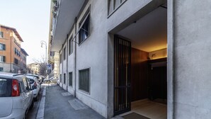 A narrow street with parked cars, a building entrance with a metal gate, and a clear sky.