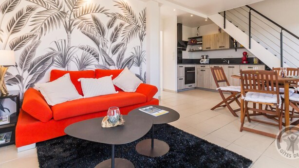 A modern living room with a red sofa, a black coffee table, and a tropical leaf wallpaper.
