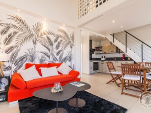 A modern living room with a red sofa, a black coffee table, and a tropical leaf wallpaper. - Bright duplex with seaside terrace (Barneville-Carteret)