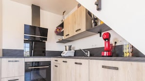 A modern kitchen with light wood cabinets, a black countertop, and a red coffee machine.
