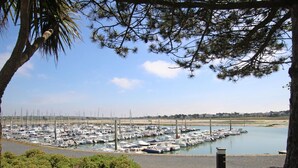 A marina with numerous boats docked, surrounded by greenery and a clear sky.